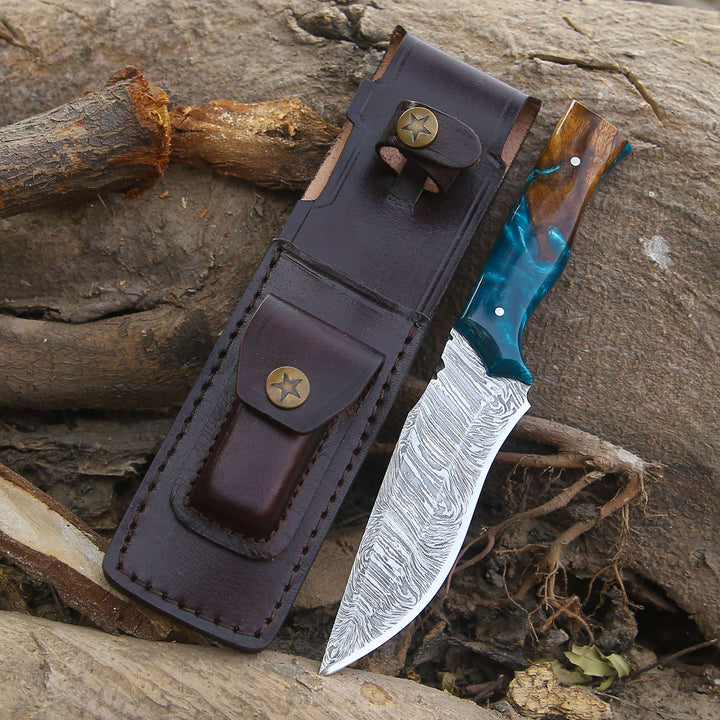 Knife with a wooden handle and blue blade in a leather sheath on a rocky surface