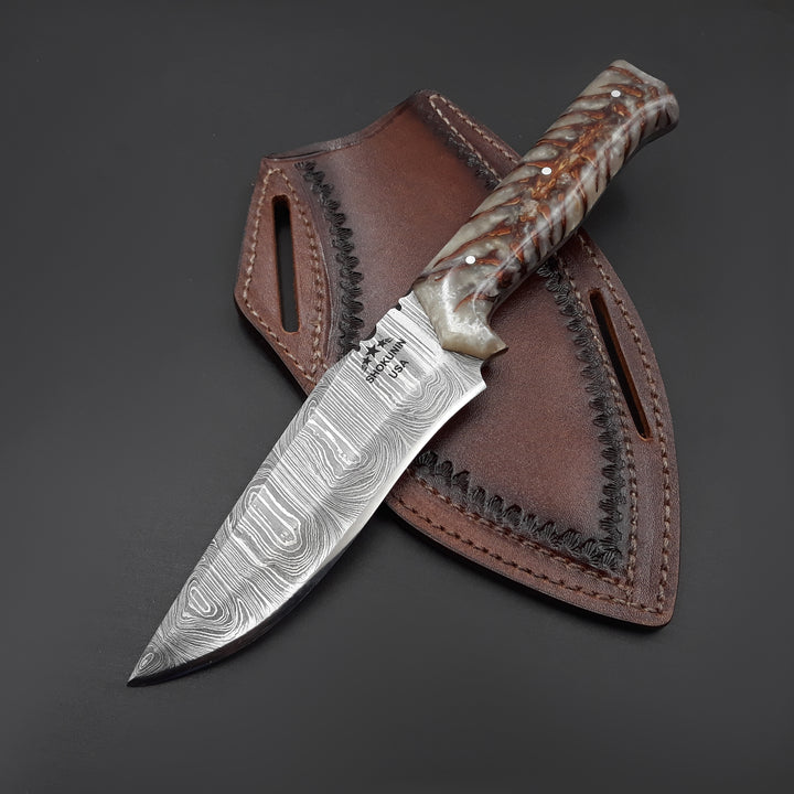 Knife with a decorative blade and brown handle in a leather sheath on a dark background