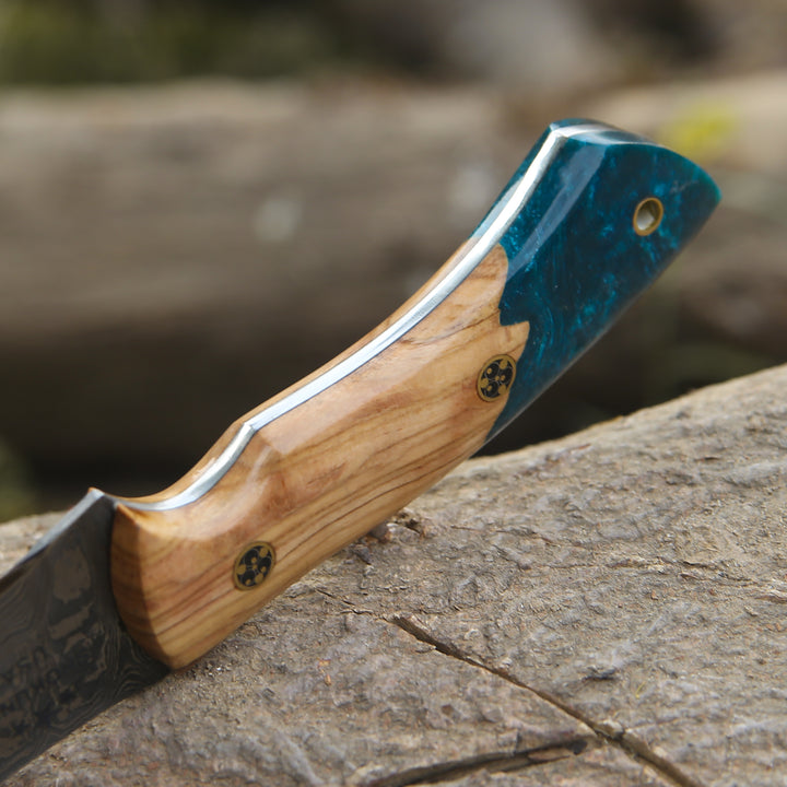 Folding knife with wooden handle and blue blade on a stone surface